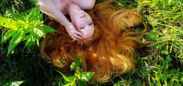 美しい若いセクシーな赤毛の女性の肖像画 彼女の赤い髪は花の中に広がり 彼女の肩を持つ緑の牧草地にリラックスして横たわって 夏の太陽と新鮮な空気を楽しんで コピースペース — ストック写真