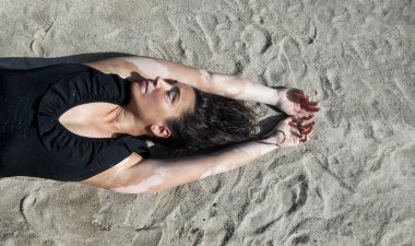 Güzel esmer olgun bir kadının portresi. Vitiligo pigment hastalığı ve uzun siyah saçları var. Plajda siyah mayo giymiş, plajda yatıyor.