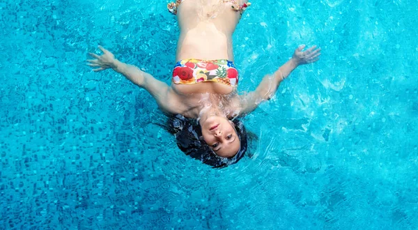 Renkli çiçekli bikinili, turkuaz kaplıca havuzunda yüzen, fotokopi çeken seksi esmer kadına tepeden bakan.