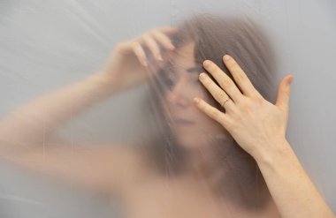 Bulanık, odak dışında güzel seksi baştan çıkarıcı kızıl saçlı baş ağrısı olan kadının karantinadaki plastik film folyosunun arkasında, boşluğu kopyala.