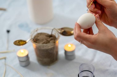 Kadın eli, Alman Sorbiya geleneğine göre beyaz bir Paskalya yumurtası boyar. İğne başlı, eritilmiş arılar ve çay mumu mumuyla, kopyalama alanı ile.
