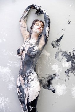 Tamamen beyaz ve siyah renkli boyayla kaplanmış genç seksi kadın stüdyo duvarının önünde poz veriyor ve gururla muhteşem kadın vücudunu gösteriyor.