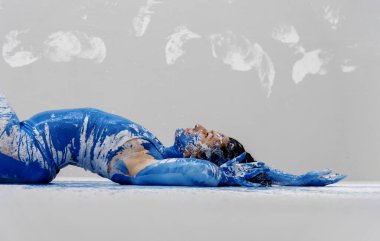 Seksi, baştan çıkarıcı, iç çamaşırlı kadın, sanatsal olarak soyut mavi ve beyaz boya ile boyanmış, renkli boyanmış zemine uzanmış, kollarını kaldırmış, arka planda beyaz izler,