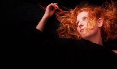 Güzel, baştan çıkarıcı, seksi, siyah arka planda kızıl saçlı bir kızın portresi. Uzun kıvırcık saçlı, kızıl saçlı güzel bir kadın. Eline şaşı bakıyor.
