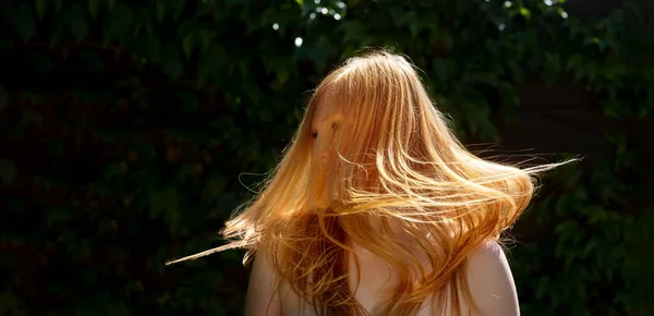 年轻美丽的红头发女子性感的性感画像在阳光下摇曳着飘扬的红头发 背景是深绿色的常春藤 复制空间 — 图库照片