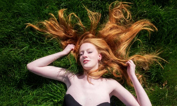 年轻性感红头发女人美丽的头像 躺在春日的争抢中 夏日的阳光 悠闲地躺在绿茵的草地上 长长的红头发飘扬在头顶上 复制着空间 — 图库照片
