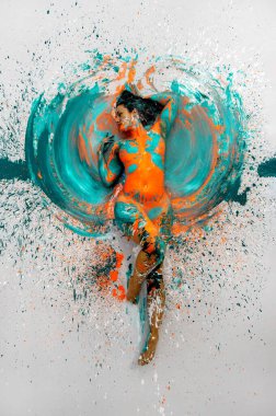 top view to expressive sexy naked woman lying elegant on the floor in turquoise blue orange color abstractly painted bodypainting woman on the splashed ground, copy space clipart
