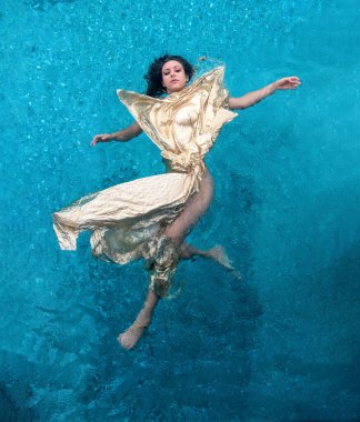 Top view of a beautiful young sexy mermaid woman jumps swimming in an extravagant golden robe through the blue water of the pool like an alien goddess, copy space