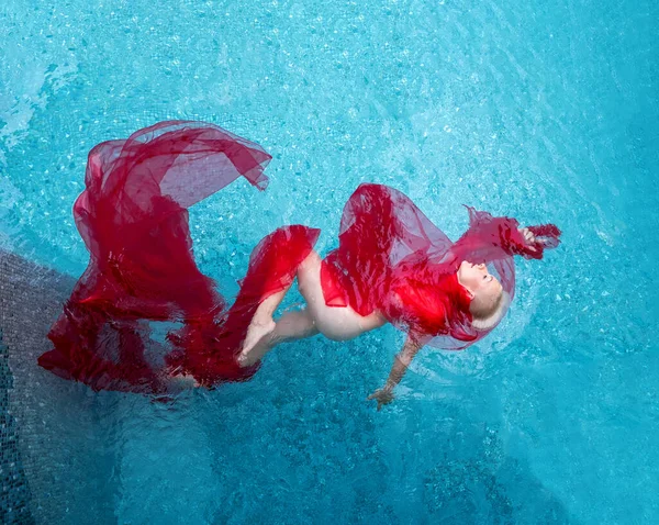 美しいセクシーな若いブロンドの女性へのトップビューは スイミングプールのターコイズブルーの水に包まれた赤い布のドレスで人魚のように浮かんでいます エレガントなエロティックな夢 ウォーターバレエ コピースペース — ストック写真