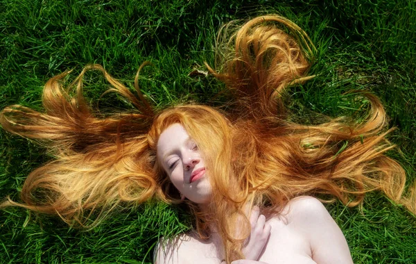 redhead portrait of a beautiful young sexy red-haired woman, lying in the spring sun, relaxing on the green grass, the red hair draped freely around the head.