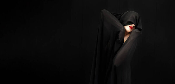 red made up mouth of female beauty model covered with black fabric on black background, wide banner portrait, copy space