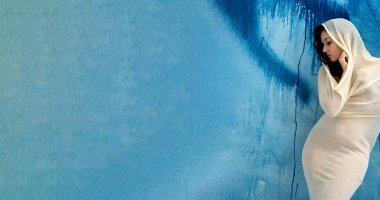 wide banner portrait of proud elegant woman in bright full body dress, wrapped in a big transparent stocking dress cloth, stands as a modern sculpture, blue background, copy space