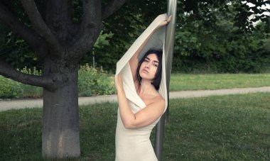 Geniş tabelalı seksi zarif kadın portresi, vücudu uzun, dar beyaz elbiseye sarılı, bükülmüş çelik çubuğa, kopyalama alanına.