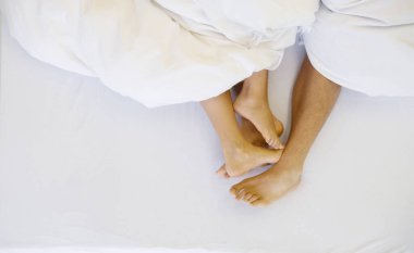 Dört bacak ve ayak, yakın çekim, yukarıdan güzel bir çift manzarası, beyaz çarşafların altında yatma, aşıklar rahatlama, sevişme üstüne yakınlık, sevgili uykusu, kopyalama alanı.