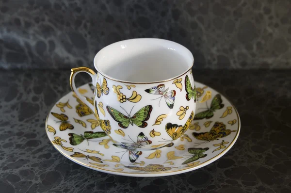 Butterfly on antique teacup on a dark background — Stock Photo, Image