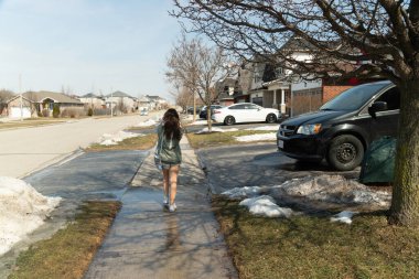 Bir kız, ilkbaharın başlarında Kanada 'da sıcak bir günde kaldırımda yürür.