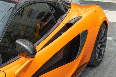 Hava girişi ve dikiz aynası olan turuncu bir spor araba parçası.