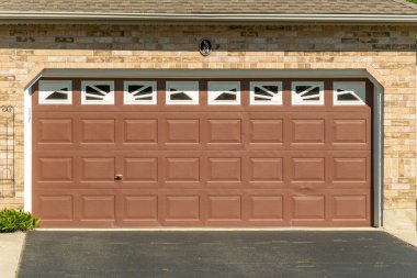 Brown garage door with white windows with asphalt at the entrance in front of the gate
