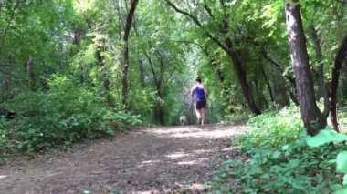 A girl with a small dog walks along the path in the park leading downhill.