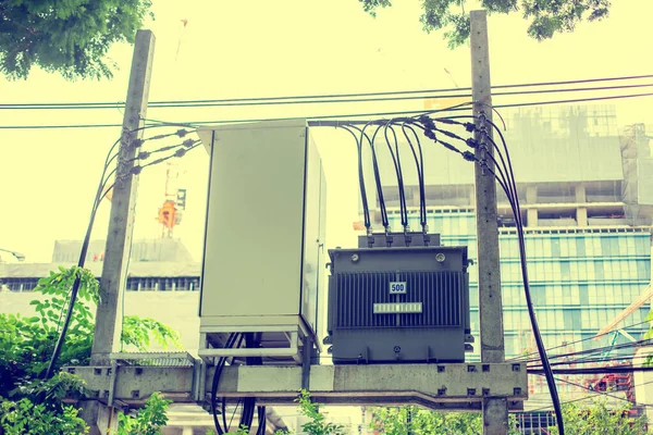 High Voltage transformer with Control box on the electric tower with blurry building under construction. Electric power.