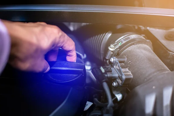 The mechanic is opening the cover to check the engine oil in car engine room.