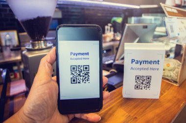 Customer hand using smart phone to scan Qr code payment tag  with blurry coffee grinder and cashier machine in coffee shop to accepted generate digital pay without money. Qr code payment concept.