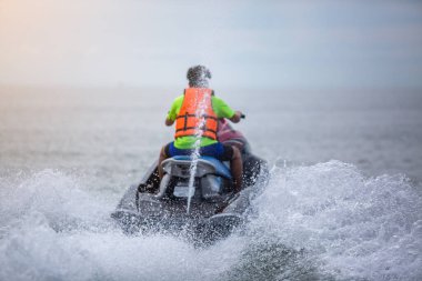 Jet ski 'deki gencin bulanık arka görüntüsü. Dalga koşucusunda kayak yapan genç bir çocuk. Genç adam tropikal denizde şahsi su aracında. Okul çocuğu için aktif yaz tatili.