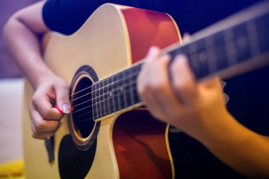Selective focus to guitar with blurry finger of musician playing acoustic classical guitar in studio room.