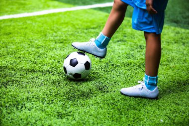 Selective focus to football ball with motion blur of kid soccer player kick it on artificial turf. Soccer player training for football match.
