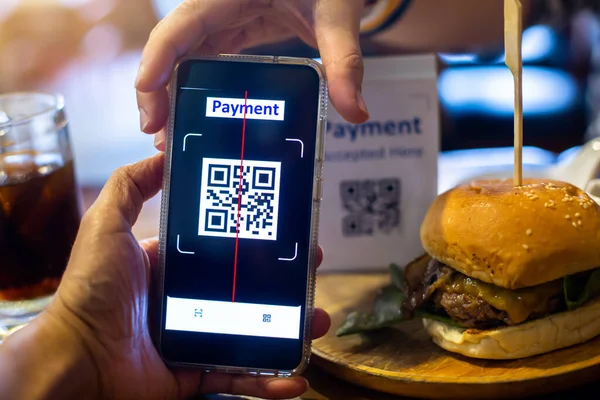 Customer hand using smart phone to scan QR code Tag with blurry hamburger in coffee shop or restaurant to accepted generate digital pay without money. Qr code payment concept.