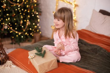 Noel arifesinde hediye getiren pijamalı mutlu küçük kız yatakta yatıyor. Çocuk yeni yıl hediyesini Noel ağacının yanında parlak ışık çelengiyle açıyor. Çocuk yatakta uyuyor. Çocuk odasında.. 