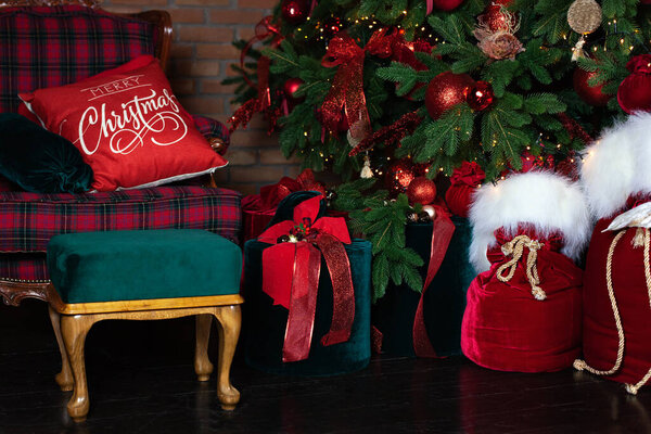 Stylish loft interior of room with Christmas fir tree and checkered armchair. Red sack santa claus with gifts near big Christmas fir. Beautiful decorated living room for Christmas. holiday celebration
