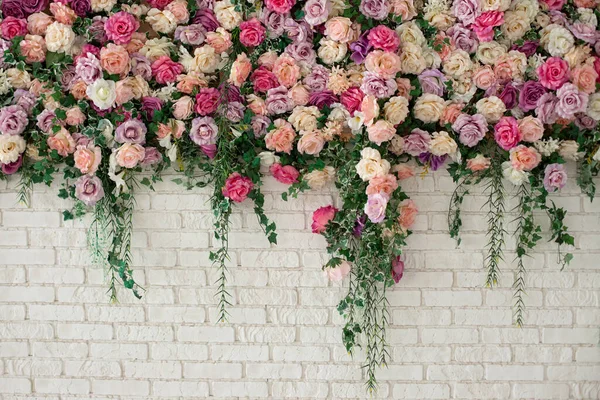 Wall with curly Flowers. Brick wall with beautiful flowers in room. Summer flowers on wall building. Beautiful decorative colorful roses and peonies on brick white wall. Interior wedding party decor.