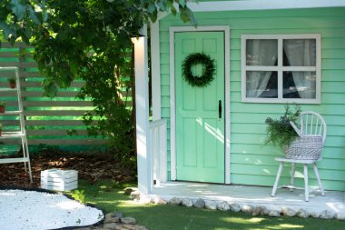 Bahar tatili için dekore edilmiş yeşil ahşap bir ev. Bahçe mobilyalarıyla birlikte verandadaki ev. İçinde sandalye ve sepet çiçekleri olan rahat bir veranda evi. Yaz bahçesinin dekorasyon evi