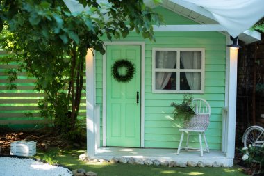 Bahar tatili için dekore edilmiş yeşil ahşap bir ev. Bahçe mobilyalarıyla birlikte verandadaki ev. İçinde sandalye ve sepet çiçekleri olan rahat bir veranda evi. Yaz bahçesinin dekorasyon evi