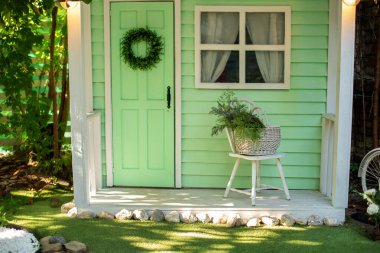 Yaz bahçesinin dışarısını dekore et. Bahçe mobilyalarıyla birlikte verandadaki ev. Bahar tatili için dekore edilmiş yeşil ahşap bir ev. İçinde sandalye ve sepet çiçekleri olan rahat bir veranda evi.