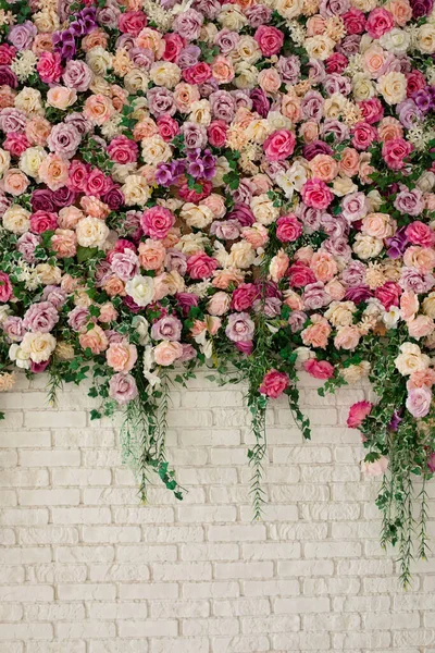 Interior wedding party decor. Spring flowers on wall building. Beautiful decorative colorful roses and peonies on brick white wall.  Wall with curly Flowers. Brick wall with beautiful flowers in room