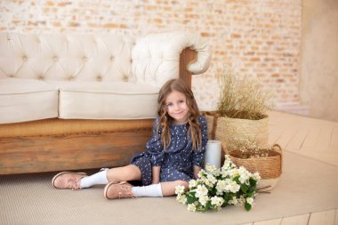 Bir buket yasemin çiçeğiyle gülümseyen kıvırcık saçlı kız sonbahar oturma odasındaki kanepede oturur. İskandinav iç mimarisi. Kutlama. Anneler Günü. Anne için bir buket çiçekli çocuk.