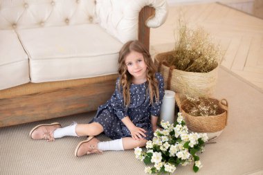 Bir buket yasemin çiçeğiyle gülümseyen kıvırcık saçlı kız sonbahar oturma odasındaki kanepede oturur. İskandinav iç mimarisi. Kutlama. Anneler Günü. Anne için bir buket çiçekli çocuk.