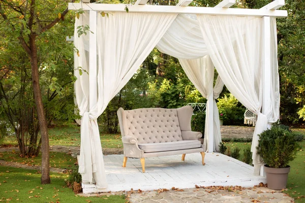 Decor outdoor terrace. Gazebo for relax outdoor. In garden there is podium on which sofa in style of Provence or rustic. Wedding decorations. Summer gazebo with flowing white curtains. Romantic alcove