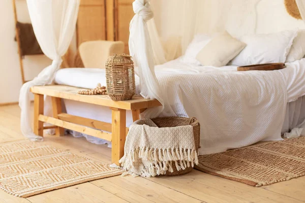 Scandinavian bedroom interior decoration with comfortable bed and pillows. Cozy room with decoration and wisker basket with plaids. hygge decor at home. Bed with flowing white curtains  in boho style.