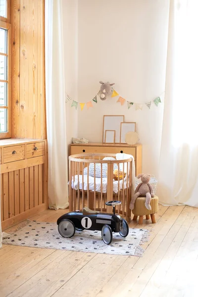 Retro style child toy racing car in children room. Modern interior of a children's bedroom. Copy space. Hygge. Kindergarten. Cozy Scandinavian lights baby room: wooden crib with bedding and plush toy