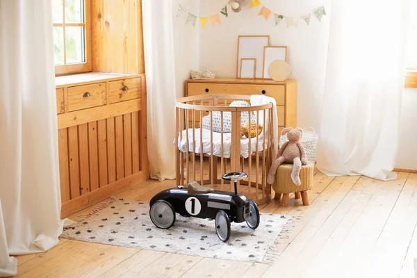Retro style child toy racing car in children room. Modern interior of a children\'s bedroom. Copy space. Hygge. Kindergarten. Cozy Scandinavian lights baby room: wooden crib with bedding and plush toy