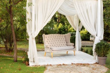 Açık hava terası. Dışarıda dinlenmek için çardak. Bahçede, Provence tarzı veya kırsal tarzında kanepe olan bir podyum var. Düğün süslemeleri. Beyaz perdeleri akan yaz çardağı. Romantik oyuk