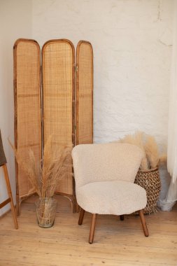 Boho tarzında ev işleri. İç dizaynı bohem tarzı oturma odasında tasarlanmış beyaz koltuk, sepet, vazoda kurumuş çiçekler, ekose ve dekoratif merdivenli ahşap basamaklar.. 