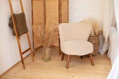  Boho tarzında dekorasyon ayrıntıları. İç dizaynı bohem tarzı oturma odasında tasarlanmış beyaz koltuk, sepet, vazoda kurumuş çiçekler, ekose ve dekoratif merdivenli ahşap basamaklar..