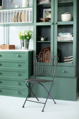 Mobilya ve dekorasyonlu yeşil mutfak. Mutfakta demir siyah sandalye. Tahta masa üstünde buket beyaz çiçekler. Duvarın yanında güzel buket laleler. Mutfak aletleri, bulaşıklar ve tabaklar. 