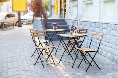 Masaları ve sandalyeleri olan boş bir kafe. Restoranın dışındaki caddede. Vazodaki çiçekler masada. Yazın Avrupa 'da bir kafede mobilya. Cafe masaları olan eski, rahat bir cadde.