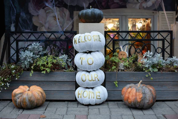 Cozy scary porch of the house with orange and white pumpkins in fall time. Halloween design home. Street decoration thanksgiving. House entrance decorated for autumn holidays.