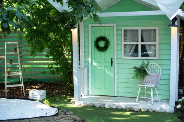 Yaz bahçesinin dışarısını dekore et. Bahçe mobilyalarıyla birlikte verandadaki ev. Bahar tatili için dekore edilmiş yeşil ahşap bir ev. İçinde sandalye ve sepet çiçekleri olan rahat bir veranda evi.